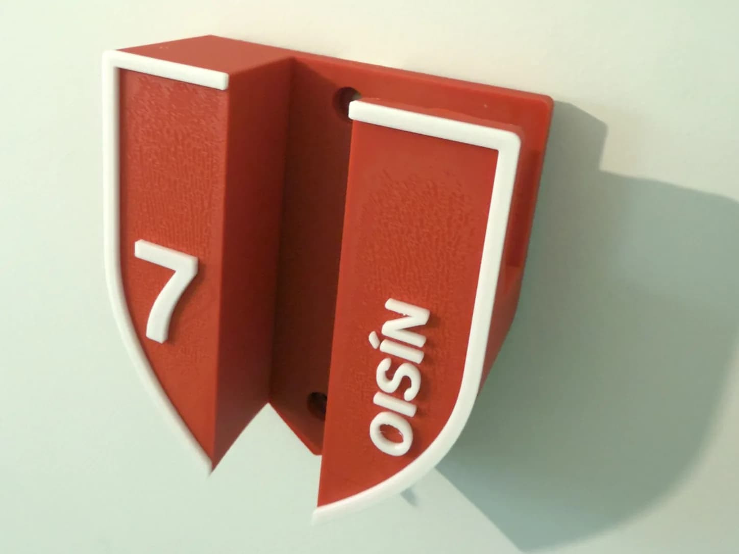A personalised red and white hurley holder printed by RUSH 3D, with the name OISÍN and number 7 raised on the shield