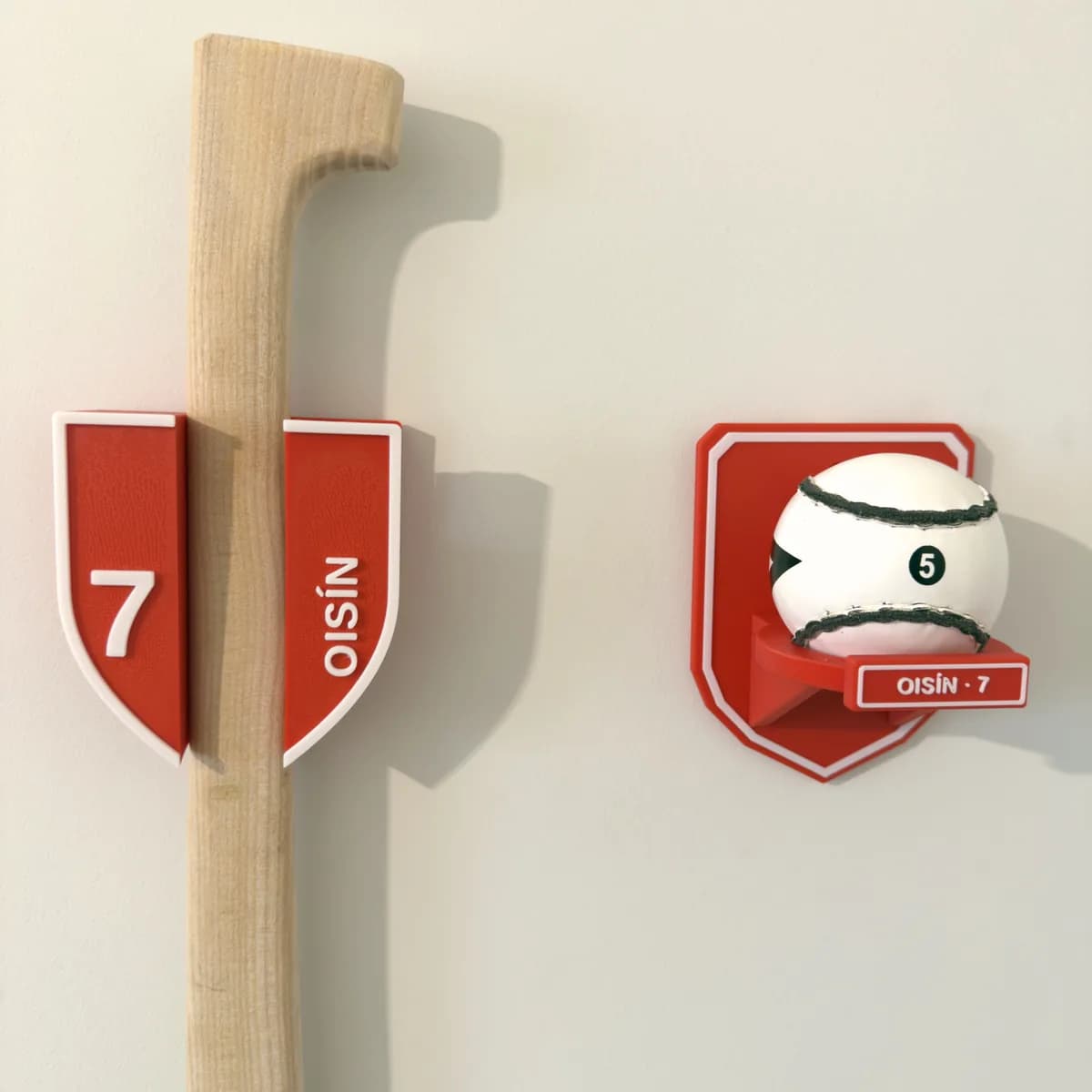 Personalised hurley holder and matching sliotar mount in Cork red and white, side by side