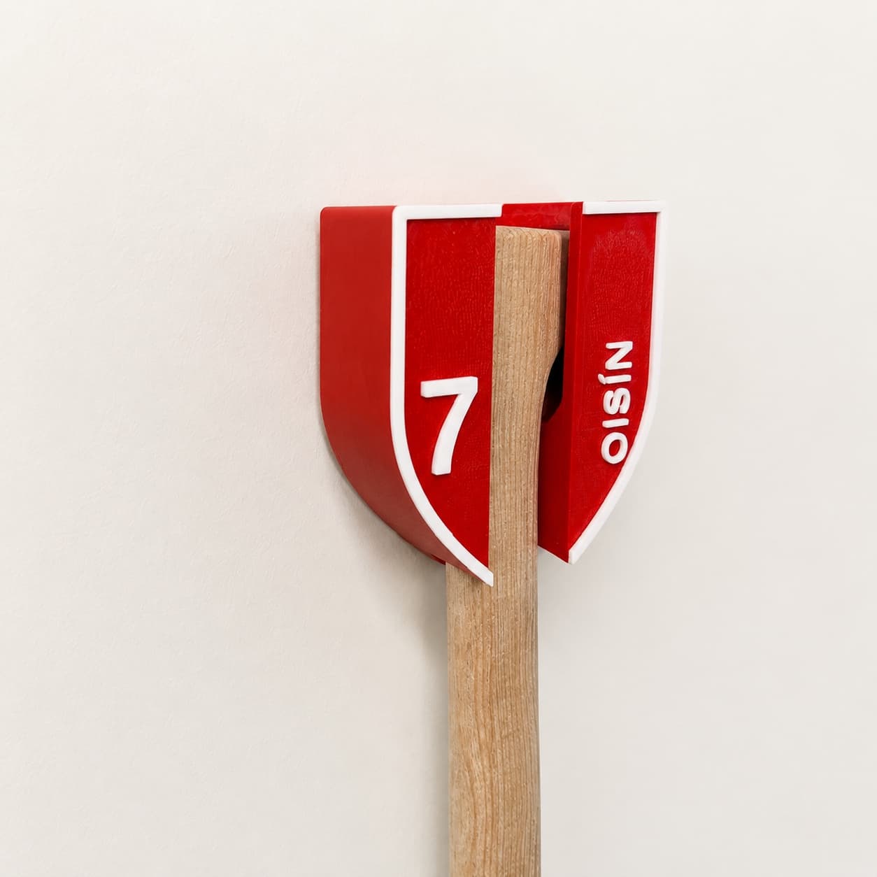 Side view of the printed Cork red and white hurley holder with a hurley seated inside, personalised with OISÍN and number 7